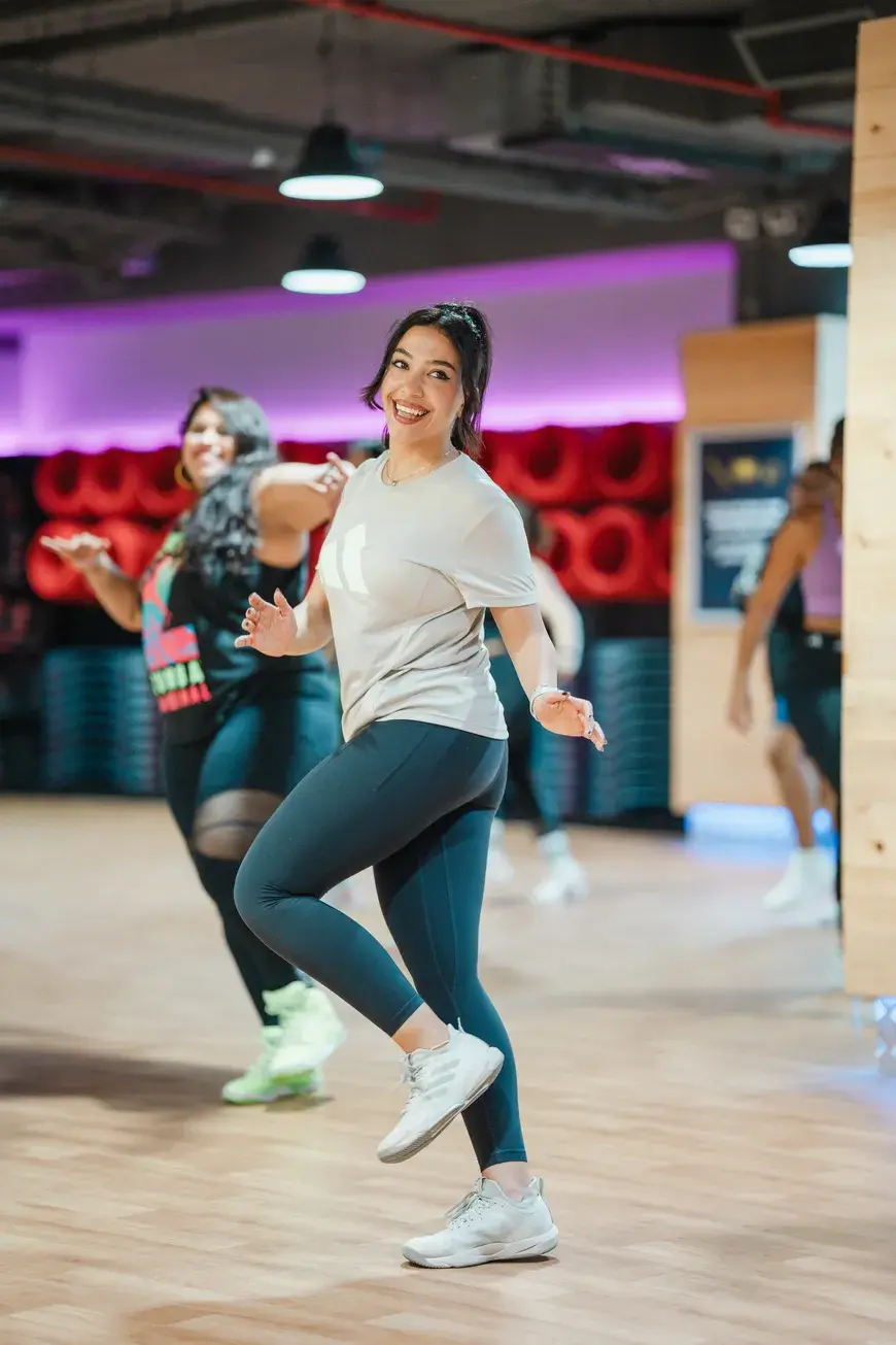 A cheerful woman mid-step during a belly dancing fitness class at GymNation, surrounded by smiling participants